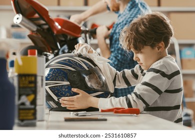 Happy cute boy helping his father in the garage, he is cleaning a helmet - Powered by Shutterstock