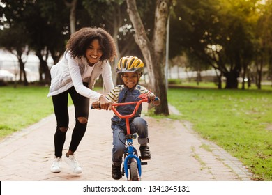 Happy cute boy learn to ride a bike with his mother. Mother teaching son to ride bicycle at park.