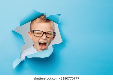 Happy cute businessboy in eyeglasses is having fun on blue background wall, climbs through a hole in the paper. Bright and funny emotions of the boy - Powered by Shutterstock