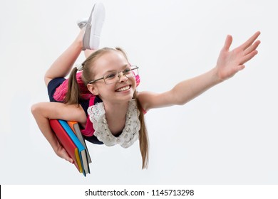 Happy cute child girl in school uniform holding books flying like a superhero. Schoolgirl with facial expression isolated on white. Concept of education, reading, back to school.