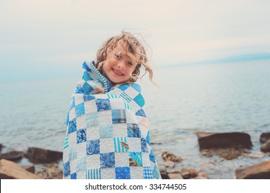 Happy Cute Child Girl At Sea Wrapped In Quilt Blanket, Warm Cozy Mood On Summer Vacation