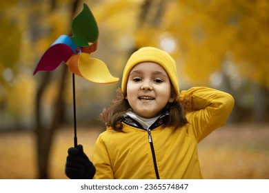 Happy cute child girl in yellow raincoat and cap walking in park or forest and play with pinwheel toy. - Powered by Shutterstock