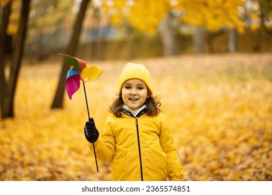 Happy cute child girl in yellow raincoat and cap walking in park or forest and play with pinwheel toy. - Powered by Shutterstock