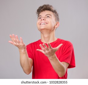 Happy Cute Child Reaching Out His Palms And Catching Something. Emotional Portrait Of Caucasian Teen Boy, Smiling. Funny Teenager Trying To Catch Something, On Gray Background.