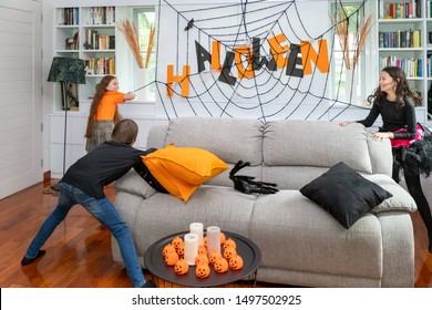 Happy Cute Children In Costume On Sofa In Living Room During Halloween Party, Boy And Girls Are Playing Running Around