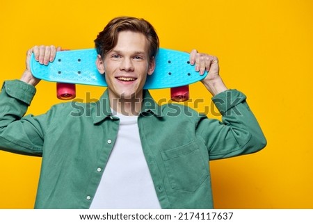 happy, cute guy posing with a skateboard against a yellow wall