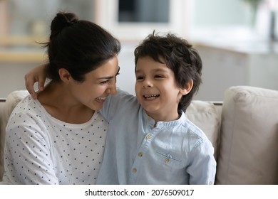 Happy cute Indian little son hugging laughing mom, sitting on lap, speaking, telling funny story. Millennial mother holding boy in arms, enjoying leisure with kid, cuddling child. Motherhood concept
