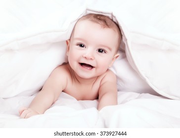 Happy and cute little baby smiling under white blanket.