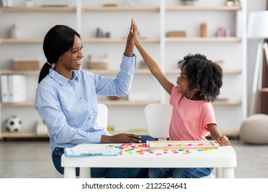 Happy Cute Little Black Girl Giving Her Young Female Teacher High Five, African American Woman And Child Preschooler Sitting At Table Together, Learning Alphabet In Kindergarten, Celebrating Success