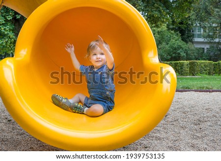 Happy cute little child boy having fun on a yellow slide outdoor in the park, sunny summer day in children playground