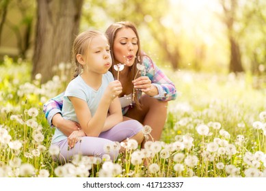 Happy cute little girl blowing dandelion with mother in the park.