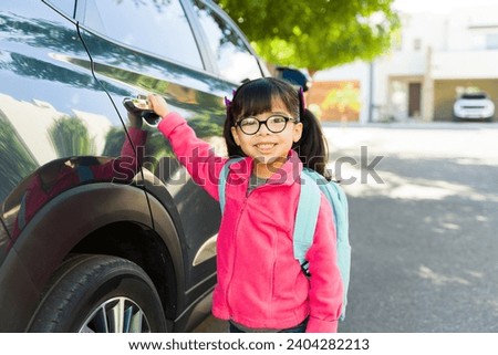 Happy cute little girl with glasses smiling with her backpack after leaving school and getting into her family car