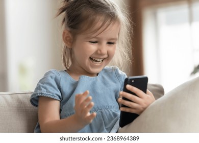 Happy cute little girl sit on couch laugh watching funny video on cellphone, smiling small preschooler kid relax on sofa have fun using modern smartphone gadget, children and technology concept - Powered by Shutterstock