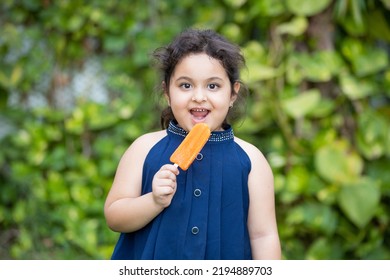 Happy cute little indian girl child enjoying ice lolly or ice cream at park.