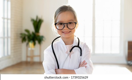 Happy cute little preschooler girl in white medical uniform and glasses act like doctor, portrait of smiling small child in whites have fun playing in hospital, engaged in funny game, career concept