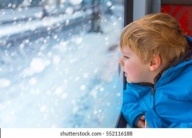 Happy Cute Little Toddler Boy Looking Out Through Window Of A Train, While It Moving. Funny Adorable Kid Traveling And Making Winter Family Vacation. Travel Concept, Child Having Fun On Railroad.