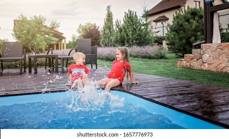 Happy Cute Sibling, Boy And Girl, Have A Fun And Splashing Each Other Near The Swimming Pool With Clear Blue Water At The Daytime, Happy Summertime, Friendly Family Weekend Concept, Outdoor Lifestyle