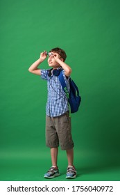 Happy Cute Smart Boy In Glasses With School Bag And Headphones. Modern Backpack. Child Tries To See Through Glasses On  Green Background. Vision Problem. Poor Vision. First Time At School. 