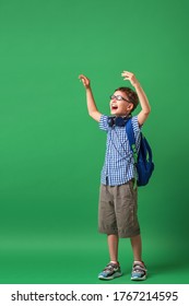 Happy Cute Smart Boy In Glasses With School Bag And Headphones. Modern Backpack. Child Tries To See Through Glasses On A Green Background. Vision Problem. Poor Vision. First Time At School. 