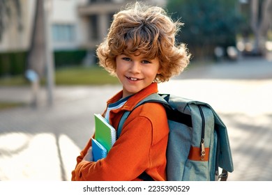 Happy cute smart boy with a stylish hairstyle with a school bag and notebooks in his hand on the street. Modern backpack. First time to school. Back to school. - Powered by Shutterstock