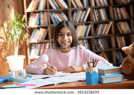 Happy cute smart hispanic indian preteen kid girl student, latin child primary school pupil studying at table at home, learning sitting at classroom desk looking at camera, schoolgirl portrait.