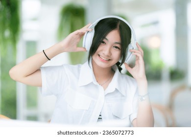 Happy of cute smiles Asian of attractive young Cute little girl wearing white wireless headphones and listening music enjoying favourite audio at the cafe on vacation at a coffee shop. - Shutterstock ID 2365072773