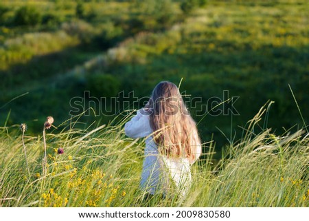    Happy cute smiling caucasian girl walking on the meadow and holding a bouquet of wildflowers.  Summer sunset.  Happy Childhood concept. Nature background. Copy space. Front focus.