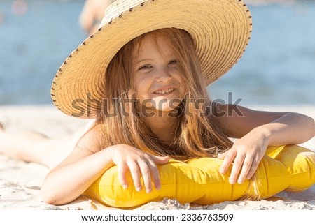 Happy cute smiling little girl in straw hat lying on the sand on a beach in a swimsuit. Summer concept