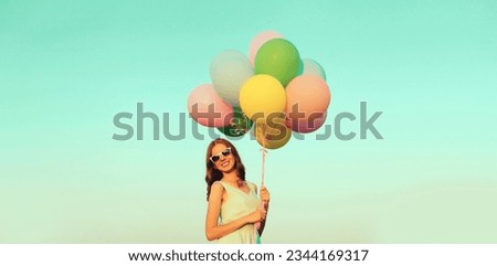 Happy cute smiling young woman with bunch of colorful balloons outdoors on blue sky background