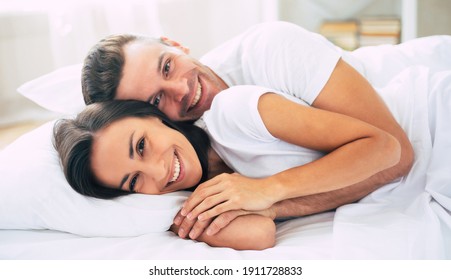 Happy Cute Young Beautiful Couple In Love Hugging Each Other And Having Fun In The Big White Bed After Dream