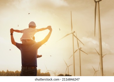 Happy dad carrying son on shoulders checking future project at wind farm site on sunset. Silhouette of father and son. 