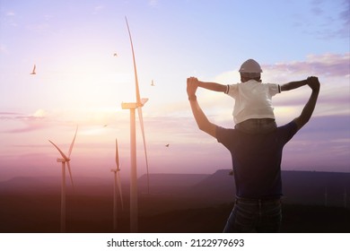 Happy dad carrying son on shoulders checking future project at wind farm site on sunset. Silhouette of father and son. 