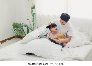 Happy Dad With Cute Daughter Holding Reading Book Together In The Bed Room, Smiling Father And Kid Girl Having Fun Being At Home Spending Time Together, Friendly Parents And Child Readers Concept.