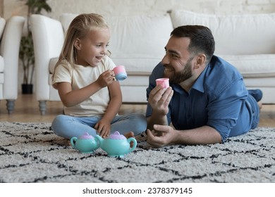 Happy dad and cute playful daughter kid relaxing on heating carpeted floor at home, playing drinking tea from small toy cups, talking, laughing, having fun, enjoying family playtime - Powered by Shutterstock