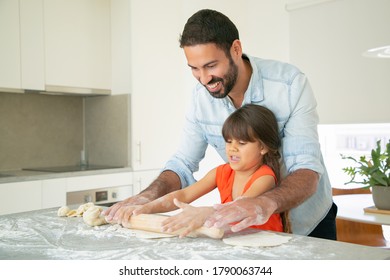 Happy Dad And Daughter Rolling Dough On Kitchen Table With Flour Messy. Father Teaching Girl To Bake Bread Or Pies. Family Cooking Concept