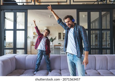 Happy Dad And His Little Son Listen To Music On Headphones And Dance At Home In The Living Room.