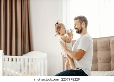 A happy dad is holding daughter in his hands and looking at her while she is drinking water. - Powered by Shutterstock