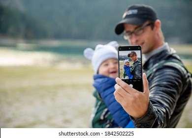 Happy Dad Keeps Baby Son In The Carrier, Hike To The Lake, Photographed On The Phone. 15.09.2020 - Tivat, Montenegro