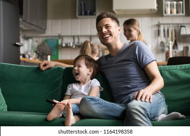 Happy Dad And Kid Son Holding Remote Control Laughing At Funny Humor Comedy Film Or Tv Show Sitting On Sofa At Home, Smiling Father Having Fun With Child Boy Watching Television Together On Weekend