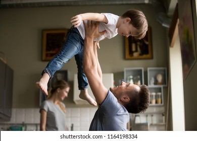 Happy Dad Lifting Son Up Having Fun Together At Home, Young Loving Father And Little Child Playing Funny Game In Living Room, Daddy Laughing Enjoying Spending Time With Kid Boy And Family On Weekend