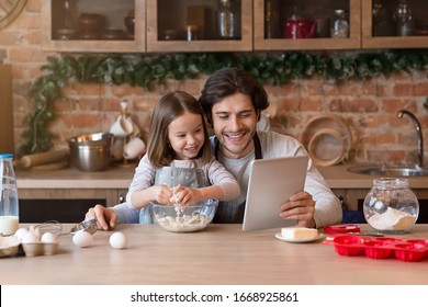 Happy Dad And Little Daughter Checking Recipe Of Dough Online On Digital Tablet While Cooking Pastry In Kitchen Together, Free Space