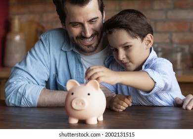 Happy Dad Teaching Smart Little Son To Save And Invest Money, Encourage Kid For Accounting, Investment, Planning Future Budget. Boy Hugging Father, Dropping Cash Into Piggy Bank. Family Economy