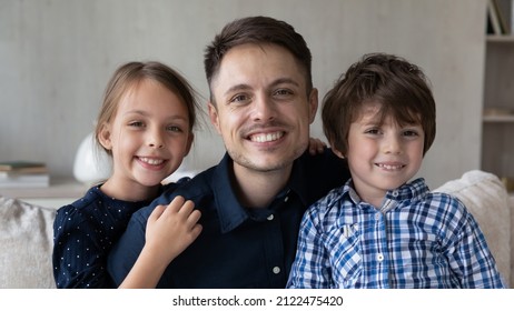 Happy dad and two little sibling kids sitting on sofa at home, looking at camera with toothy smiles. Young father and children posing for family picture together. Head shot portrait, banner