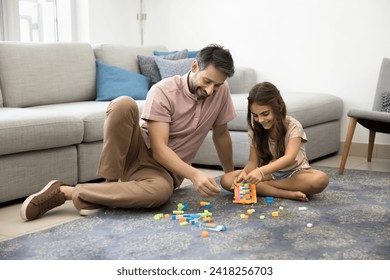 Happy daddy and cute little daughter girl constructing toy tower from building blocks, playing on warm carpeted floor, smiling, laughing, having fun on family playtime with child - Powered by Shutterstock