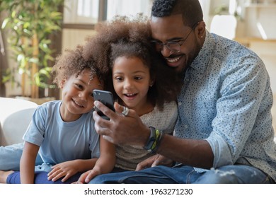 Happy daddy and excited sibling kids watching amazing content on smartphone screen together. Dad, preschooler son and daughter relaxing on couch, using mobile phone, talking to mom via video call - Powered by Shutterstock