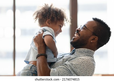 Happy daddy holding kid in arms, hugging toddler boy. African American dad enjoying being father, spending time and playing with cute preschooler son, talking to child, laughing. Parent concept - Shutterstock ID 2176074815