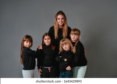 Happy Dance Team. Young And Positive Female Dance Teacher And Four Little Girls In Black Sweatshirts Looking At Camera With Smile While Standing In The Dance Studio. Choreography Concept.