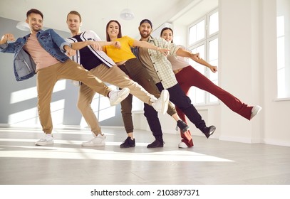 Happy dancers posing for a photo standing in a row on one leg. Cheerful friends having fun together during a dancing class. Low angle group shot of smiling young people walking in line in single file - Powered by Shutterstock