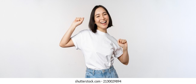 Happy Dancing Korean Girl Posing Against White Background, Wearing Tshirt