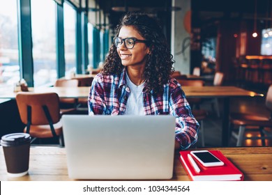 Happy Dark Skinned Female Graphic Designer In Eyewear Laughing During Working At Modern Laptop Connected To Wireless 4G Internet.Positive African American Student Sitting At Netbook In University